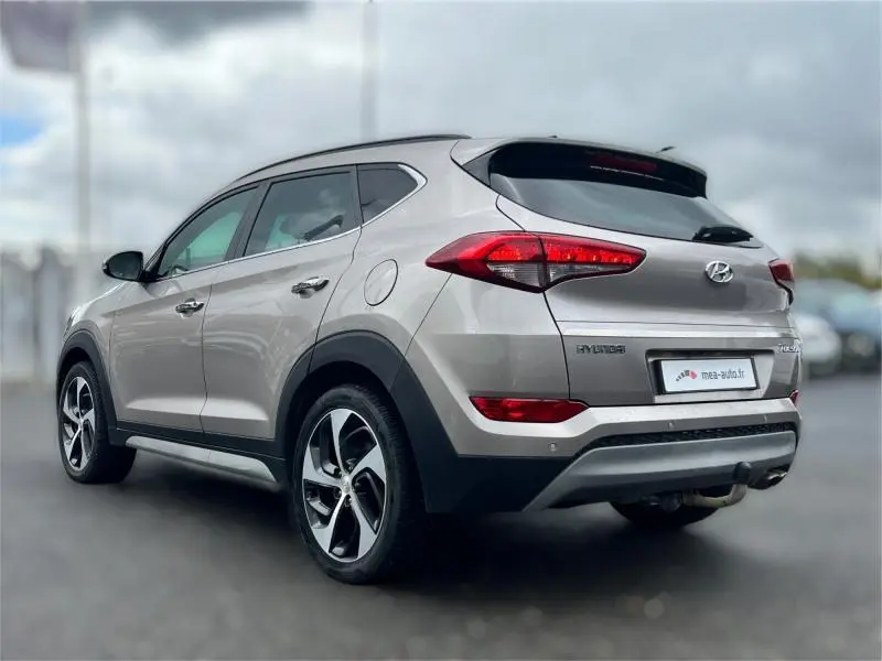 Vue 3/4 arrière droite d'un Hyundai Tucson 2017 White Sand avec jantes alu et barres de toit visibles.