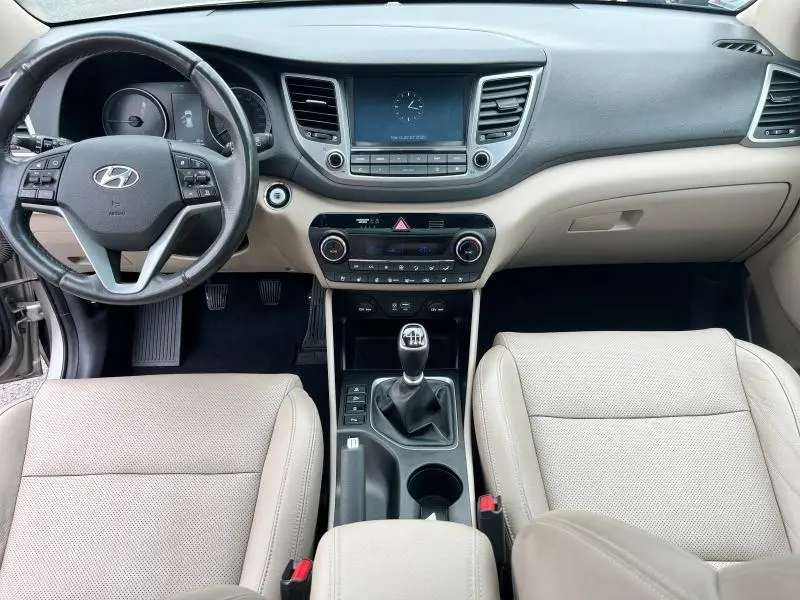 Vue intérieure avant du Hyundai Tucson 2017 avec tableau de bord noir, sièges cuir beige et levier de vitesse manuel.