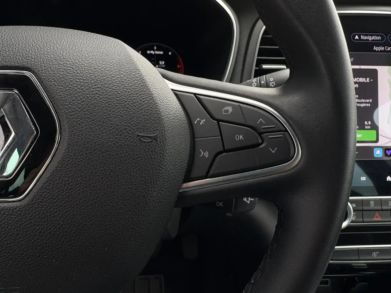 Gros plan sur le volant noir de la Renault Mégane Break 2024 avec commandes intégrées et écran tactile GPS en arrière-plan.