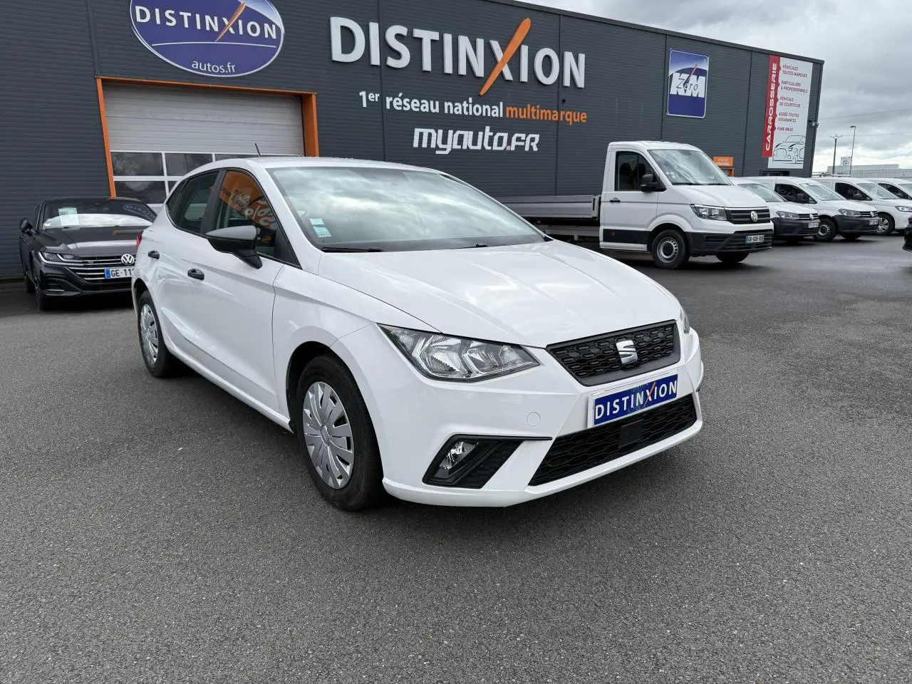 SEAT Ibiza blanc candy vue 3/4 avant droit, avec jantes enjoliveurs et rétroviseurs noirs, sur parking devant concession.