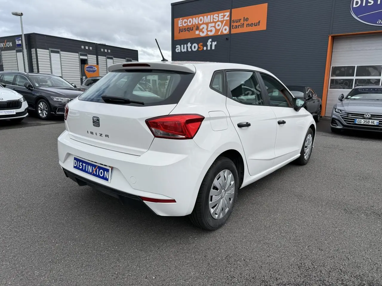 Vue 3/4 arrière droite d'une SEAT Ibiza blanche Candy 2019 avec jantes enjoliveurs et feux arrière rouges.