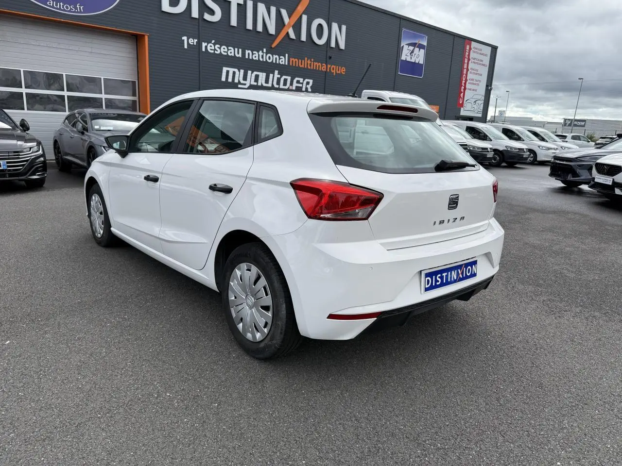 Vue 3/4 arrière droite d'une SEAT Ibiza blanche Candy 2019 avec jantes acier et enjoliveurs sur parking extérieur.