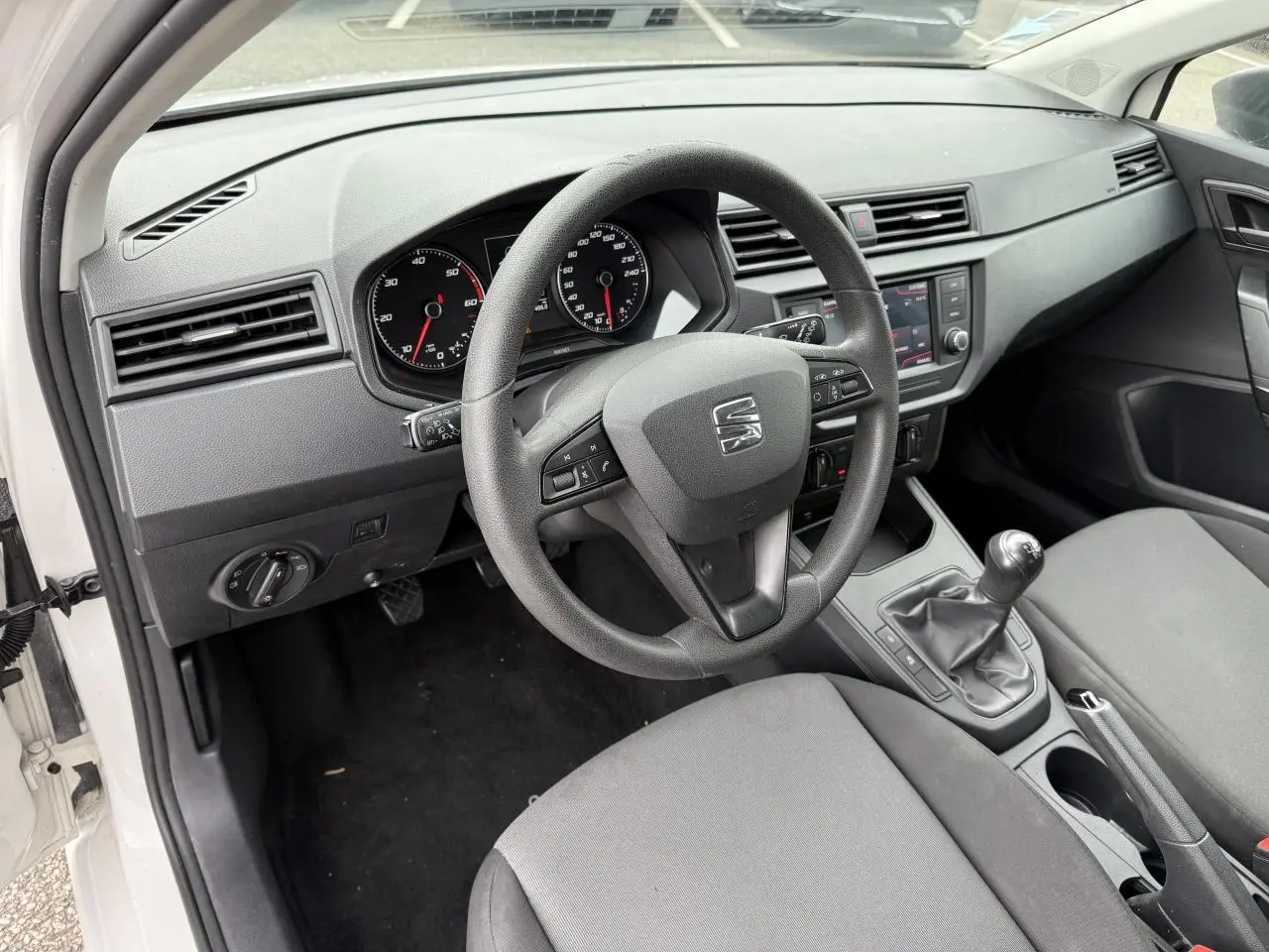 Vue intérieure côté conducteur d'une SEAT Ibiza blanche de 2019, volant multifonction et tableau de bord avec écran tactile.