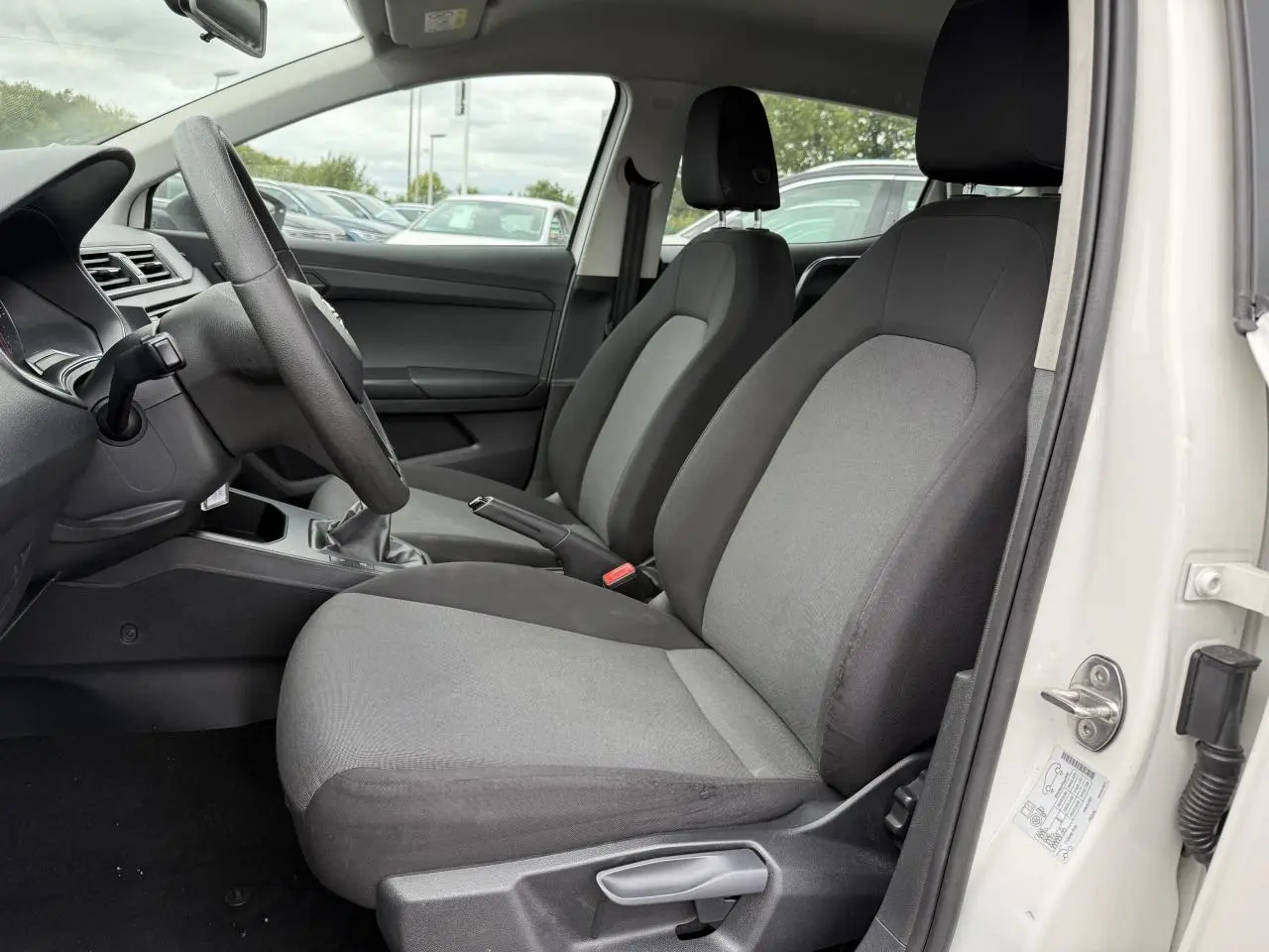 Vue intérieure côté conducteur de la SEAT Ibiza blanche, montrant les sièges avant gris et le volant multifonction.