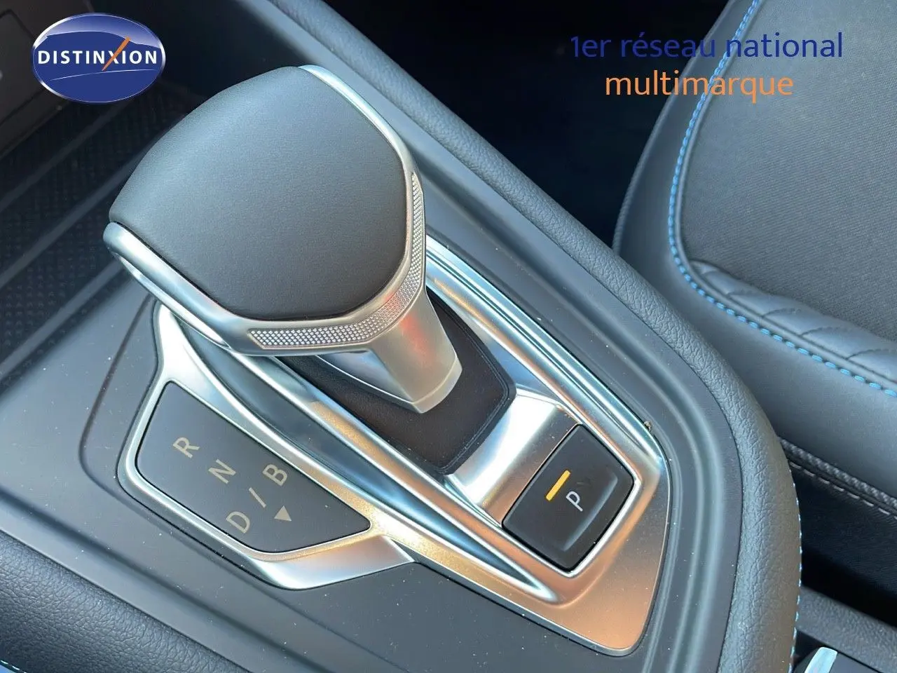 Le levier de vitesses automatique argenté et noir de la Renault Captur E-Tech hybride, avec coutures bleues visibles sur la sellerie.