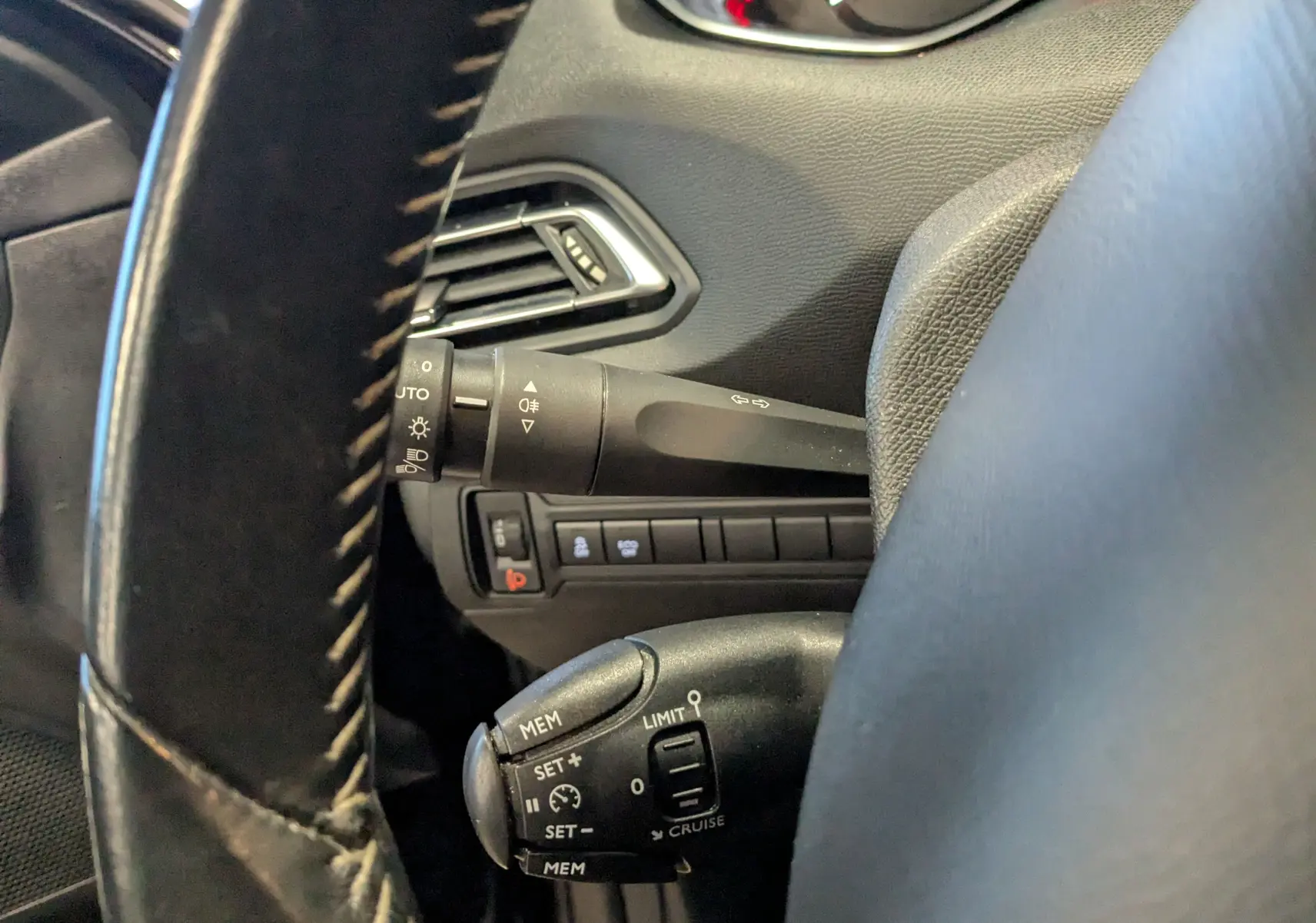 Gros plan sur la commande de régulateur de vitesse et le commodo d’éclairage à gauche du volant d’une Peugeot 308 noire.