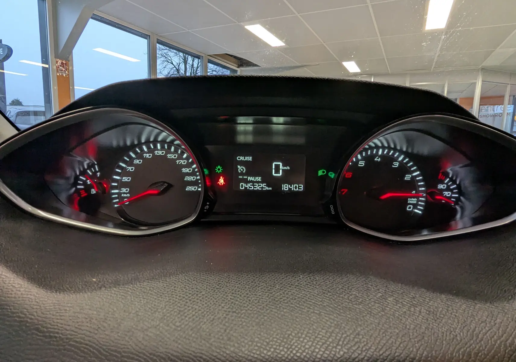 Vue rapprochée du tableau de bord de la Peugeot 308 noire, affichant le compteur de vitesse et le compte-tours allumés.