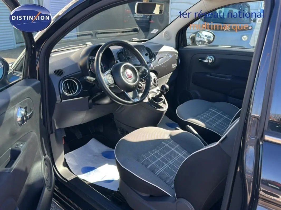 Vue intérieure côté conducteur de la Fiat 500 noire, montrant le volant, la boîte manuelle et les sièges à motifs gris.