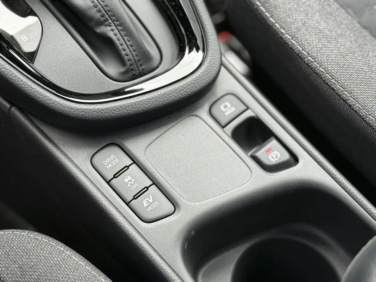 Gros plan sur la console centrale de la Toyota Yaris Cross 1.5 Hybrid 116 Design, montrant les boutons de mode de conduite et frein électrique.