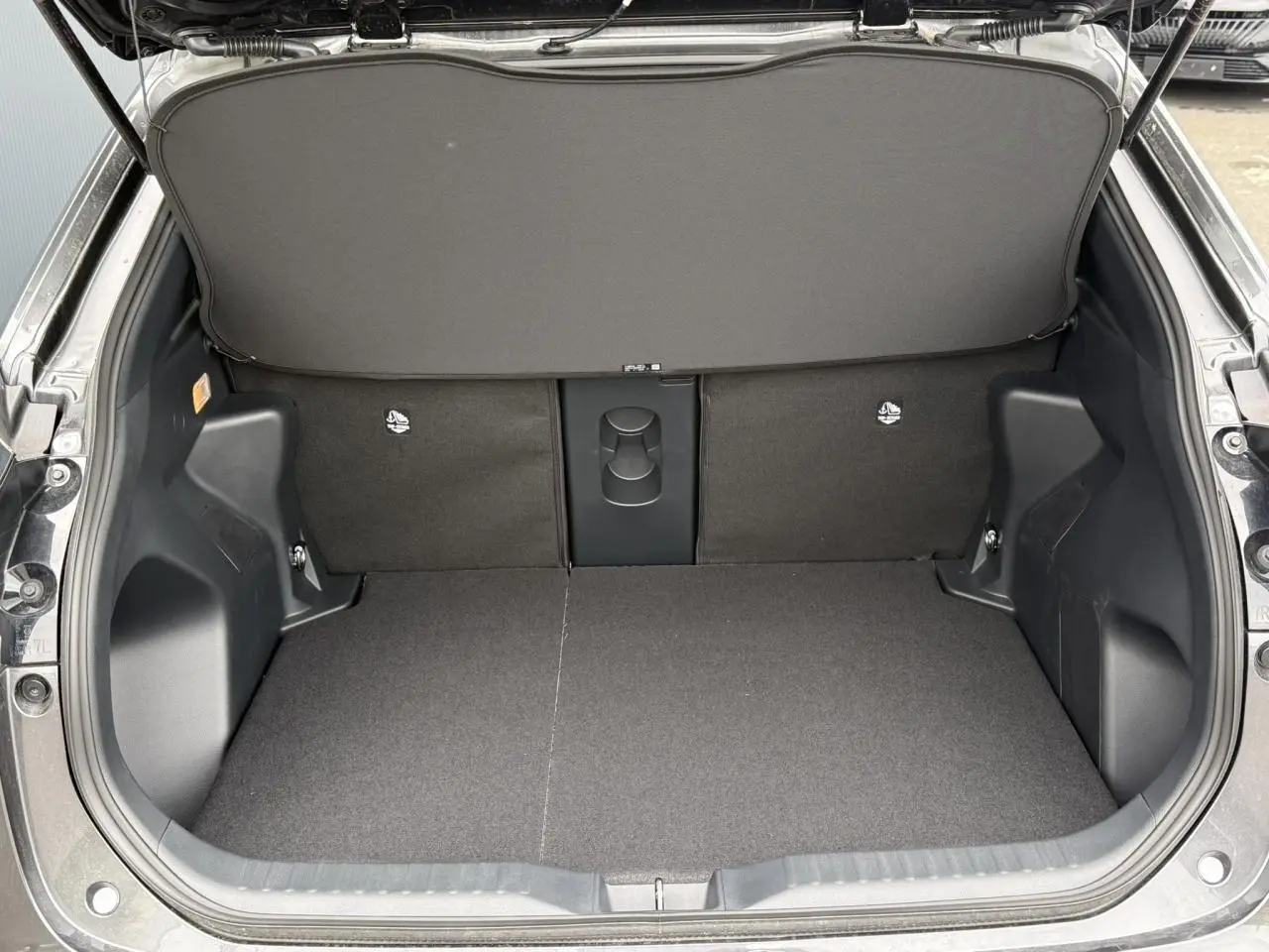 Coffre ouvert vu de l'arrière d'une Toyota Yaris Cross gris Atlas, montrant un plancher plat et un cache-bagages relevé.