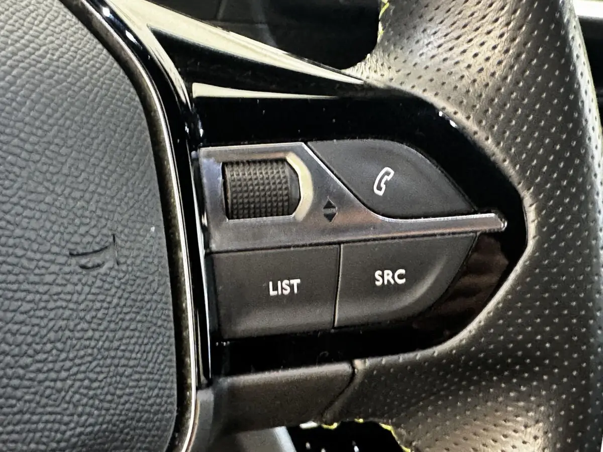 Gros plan sur les commandes multifonctions gauche du volant cuir perforé noir du Peugeot E-2008 électrique GT Pack 2021.