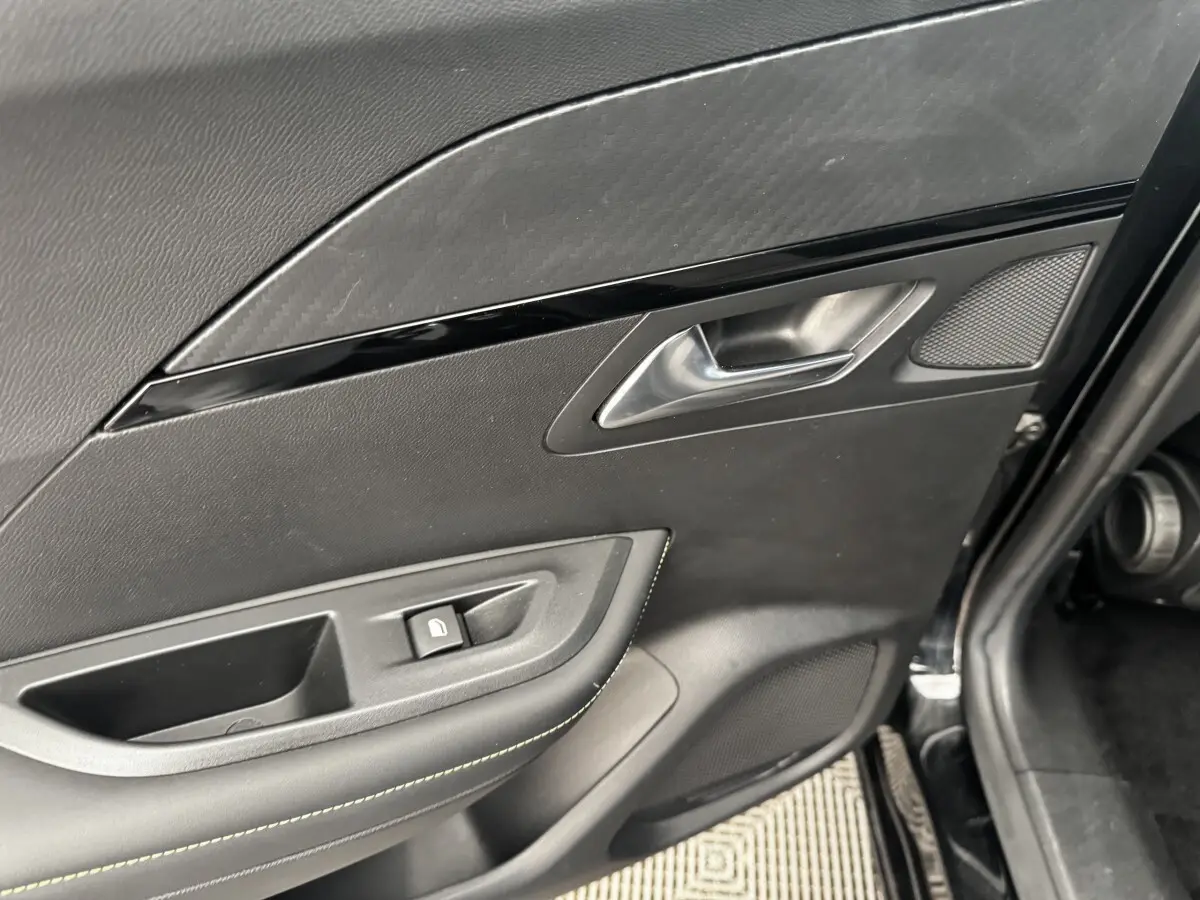 Gros plan sur la porte intérieure côté gauche noire du Peugeot E-2008 électrique GT Pack avec poignée et bouton de verrouillage.