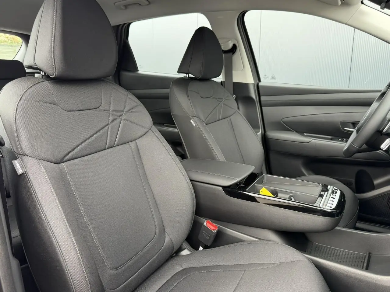 Vue intérieure côté conducteur du Hyundai Tucson 2026 avec sièges tissu gris foncé et console centrale ouverte.