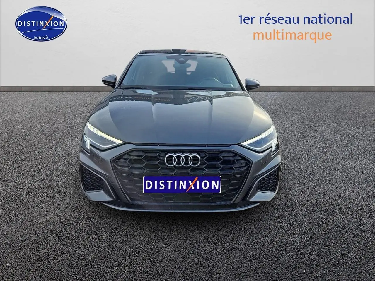 Audi A3 Sportback 45 TFSI e gris Daytona vue de face, calandre noire et phares LED allumés.