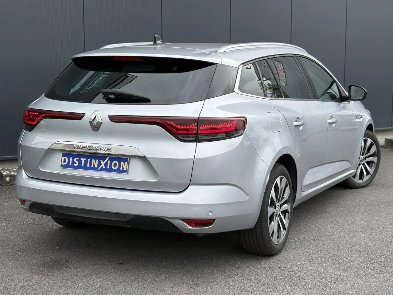 Renault Mégane Break gris Highland vue 3/4 arrière droit, feux arrière LED et jantes alliage visibles.