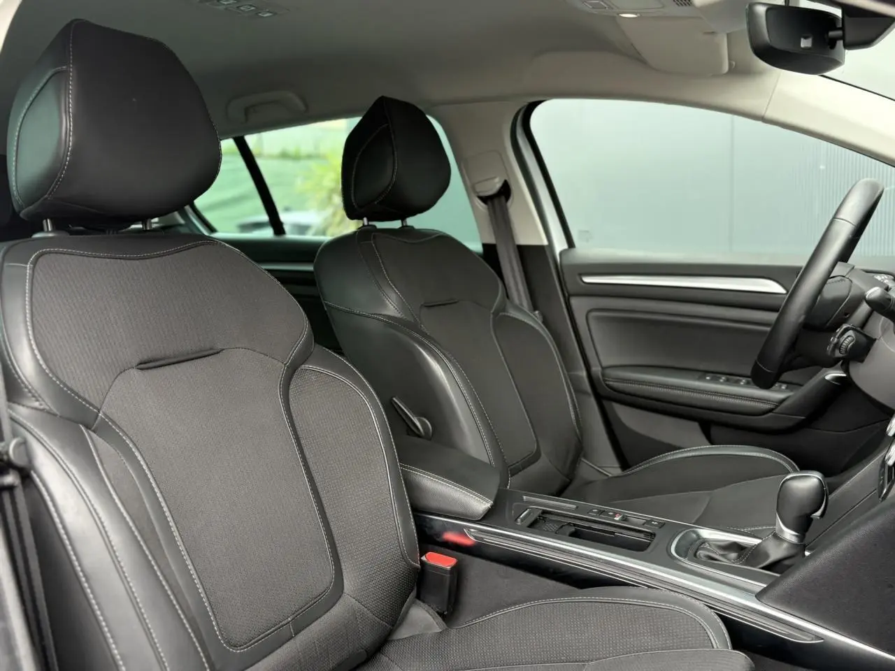 Intérieur avant de la Renault Mégane Break 2024, sièges noirs en similicuir et tissu, console centrale avec levier de vitesses.