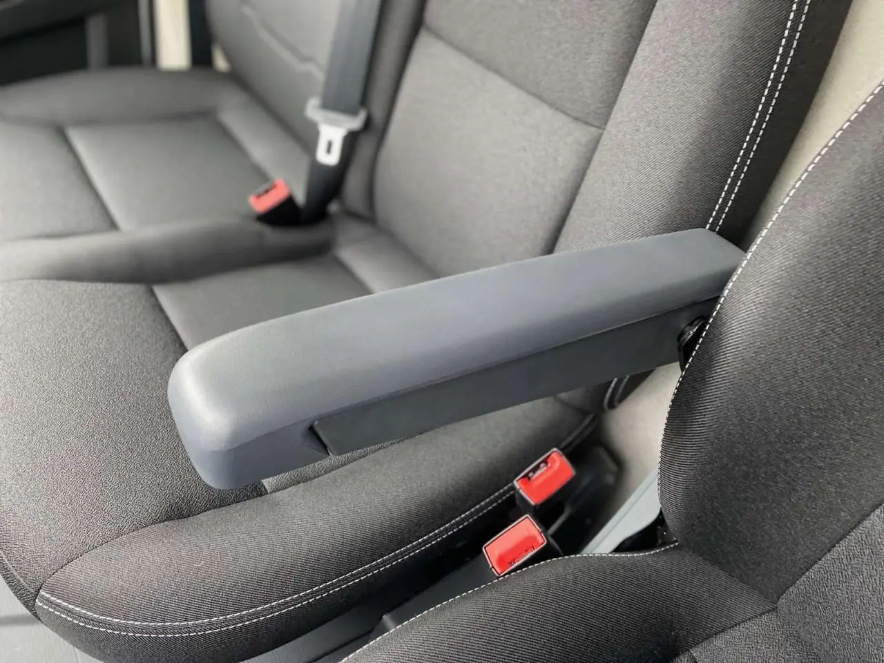 Gros plan sur l'accoudoir central relevable et la sellerie noire avec surpiqûres blanches du Citroën Jumper 2025.