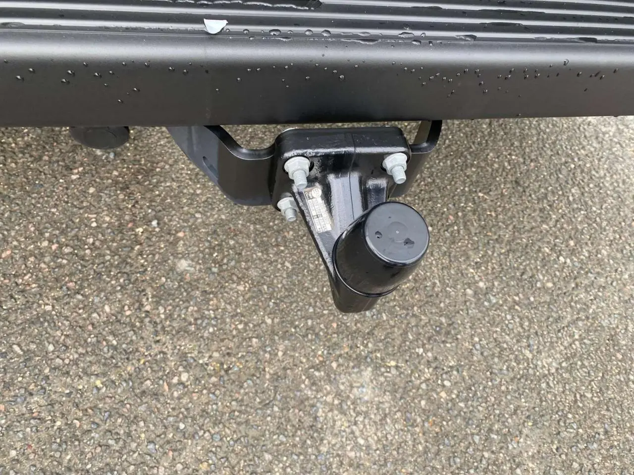 Gros plan sur le crochet d'attelage noir fixé à l'arrière d'un Citroën Jumper blanc, sur sol goudronné humide.