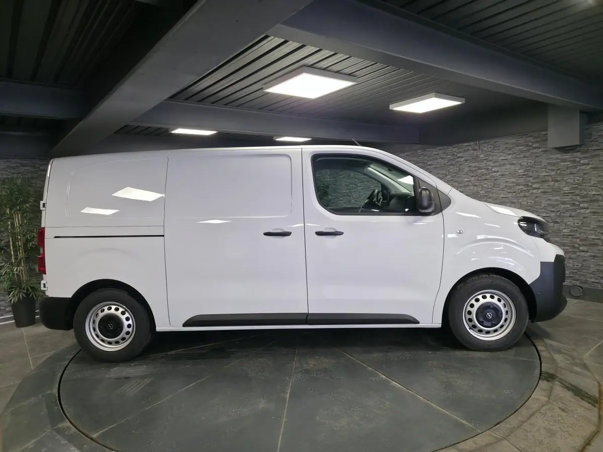 Opel Vivaro blanc en vue profil côté gauche, fourgon utilitaire avec roues tôles et poignées noires.