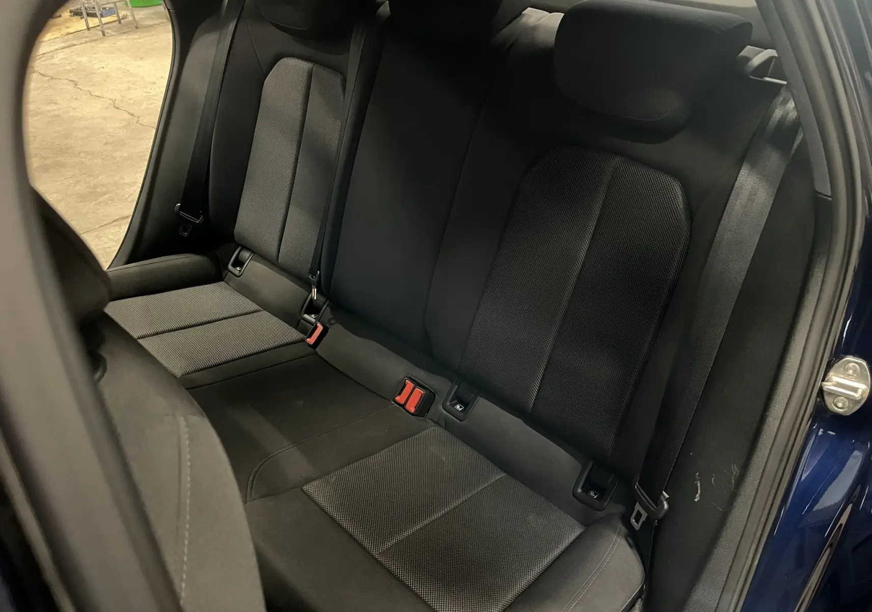 Vue intérieure de la banquette arrière noire de l'Audi A3 Sportback 30 TFSI, porte arrière bleu métallisé ouverte.