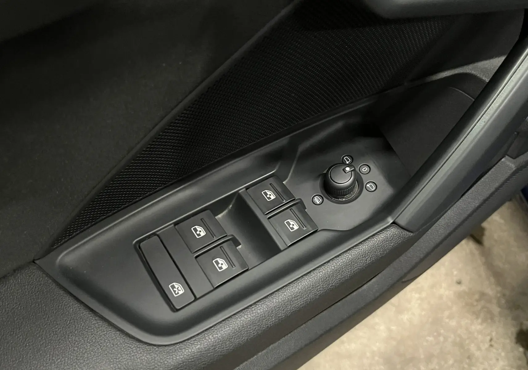 Gros plan sur les commandes des vitres et des rétroviseurs côté conducteur d'une Audi A3 Sportback bleu métallisé.