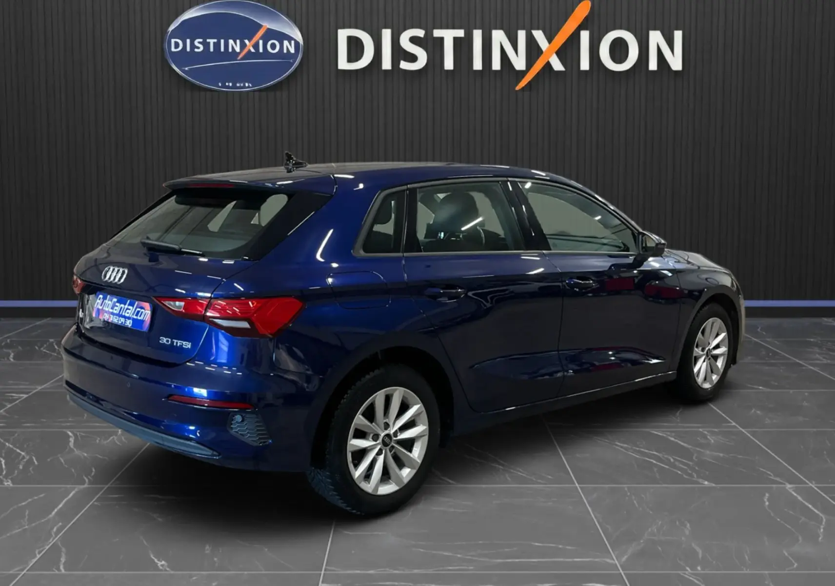 Audi A3 Sportback bleu métallisé vue 3/4 arrière droit dans un showroom avec logo Distinxion en arrière-plan.