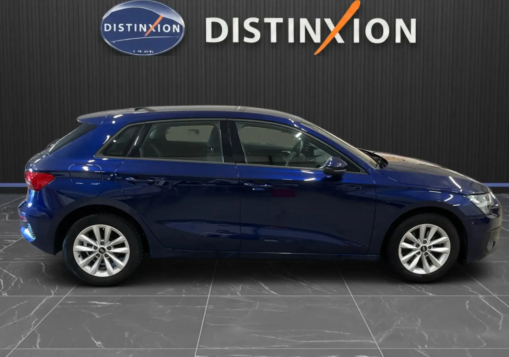 Profil latéral droit d'une Audi A3 Sportback bleu métallisé 2021, avec jantes alliage et cinq portes visibles en intérieur showroom.