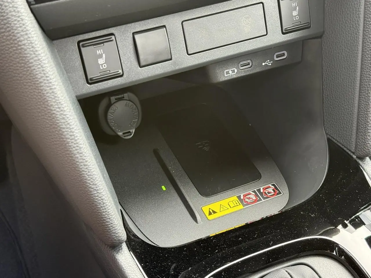 Gros plan sur la console centrale de la Toyota Yaris Cross 2026 montrant le chargeur à induction et commandes sièges chauffants.