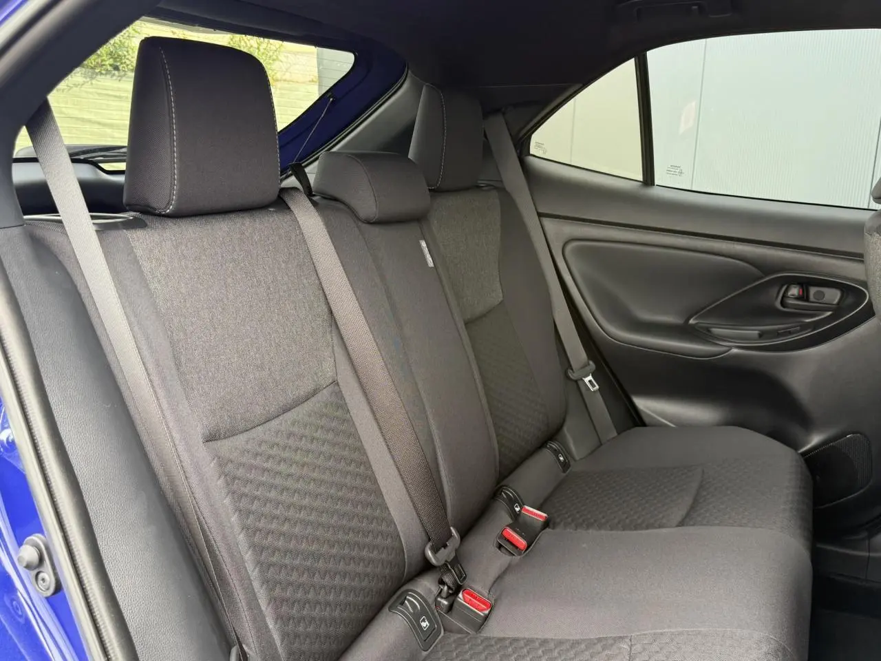 Vue latérale droite des sièges arrière noirs du Toyota Yaris Cross 1.5 Hybrid 116 Design bleu Genievre, avec ceinture de sécurité visible.