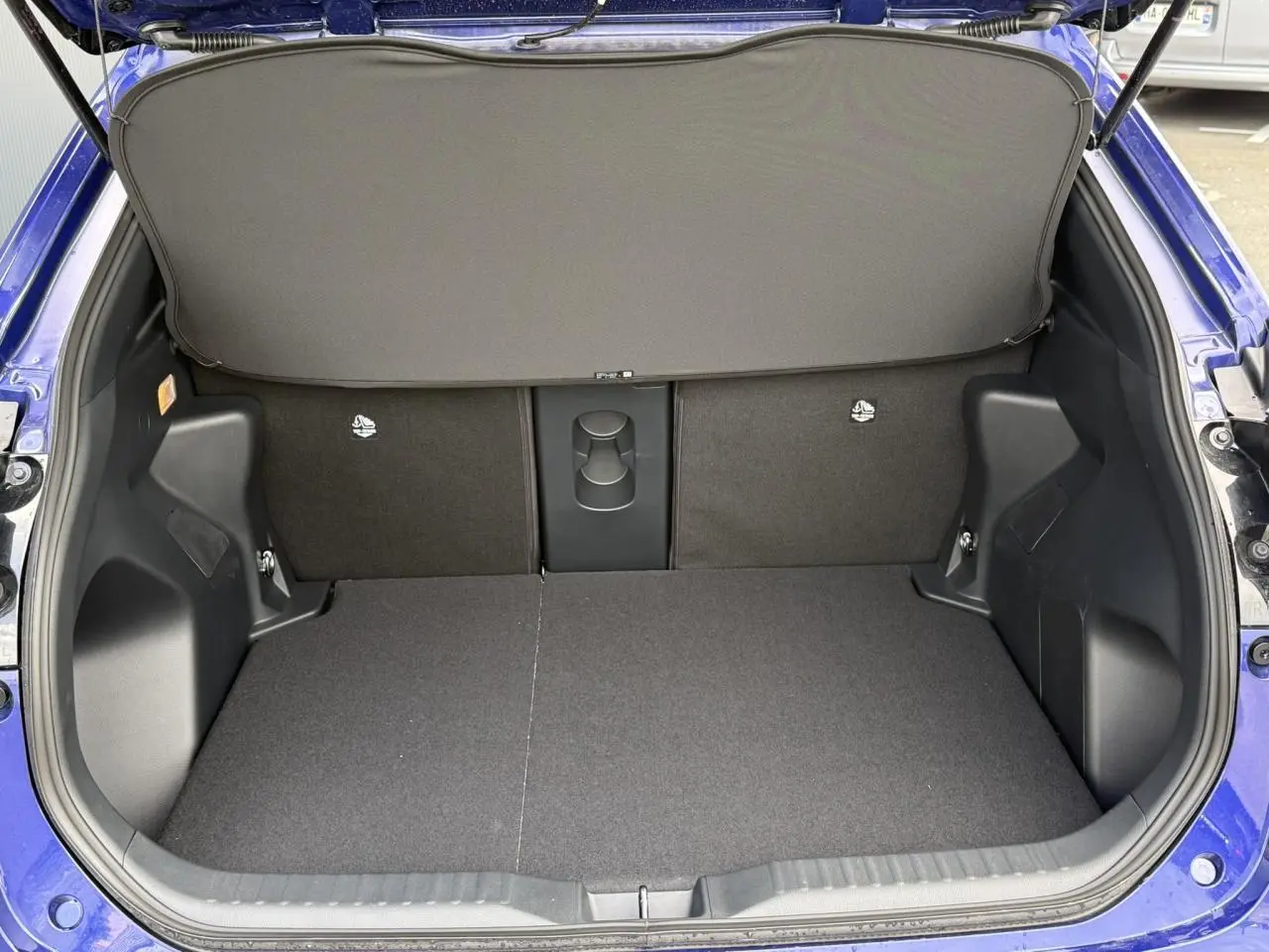 Coffre ouvert vu de l'arrière d'une Toyota Yaris Cross 1.5 Hybrid bleu Genievre avec plancher plat et cache-bagages.