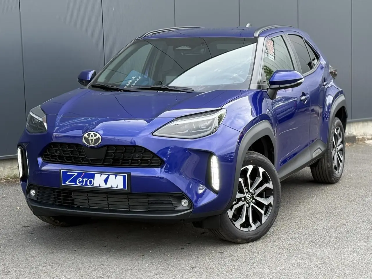 Toyota Yaris Cross bleu Genievre en 3/4 avant droit, avec feux LED verticaux allumés et jantes alliage noires.