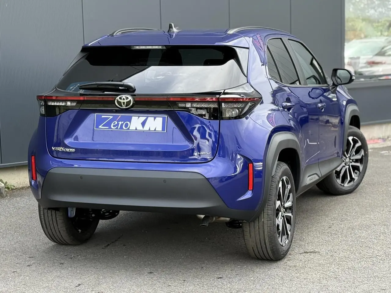 Vue 3/4 arrière droite d'une Toyota Yaris Cross 1.5 Hybrid bleu Genievre avec feux arrière LED et jantes alliage noires.