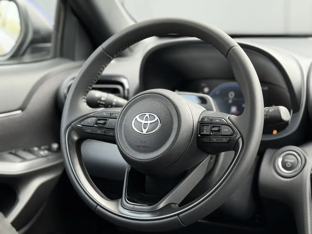 Vue rapprochée du volant cuir noir de la Toyota Yaris Cross 2026 avec commandes intégrées et tableau de bord flou.