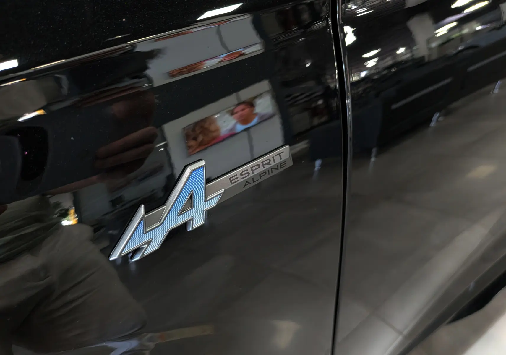 Gros plan sur l’écusson Esprit Alpine bleu et argent sur la porte noire brillante d’un Renault Austral 2026.