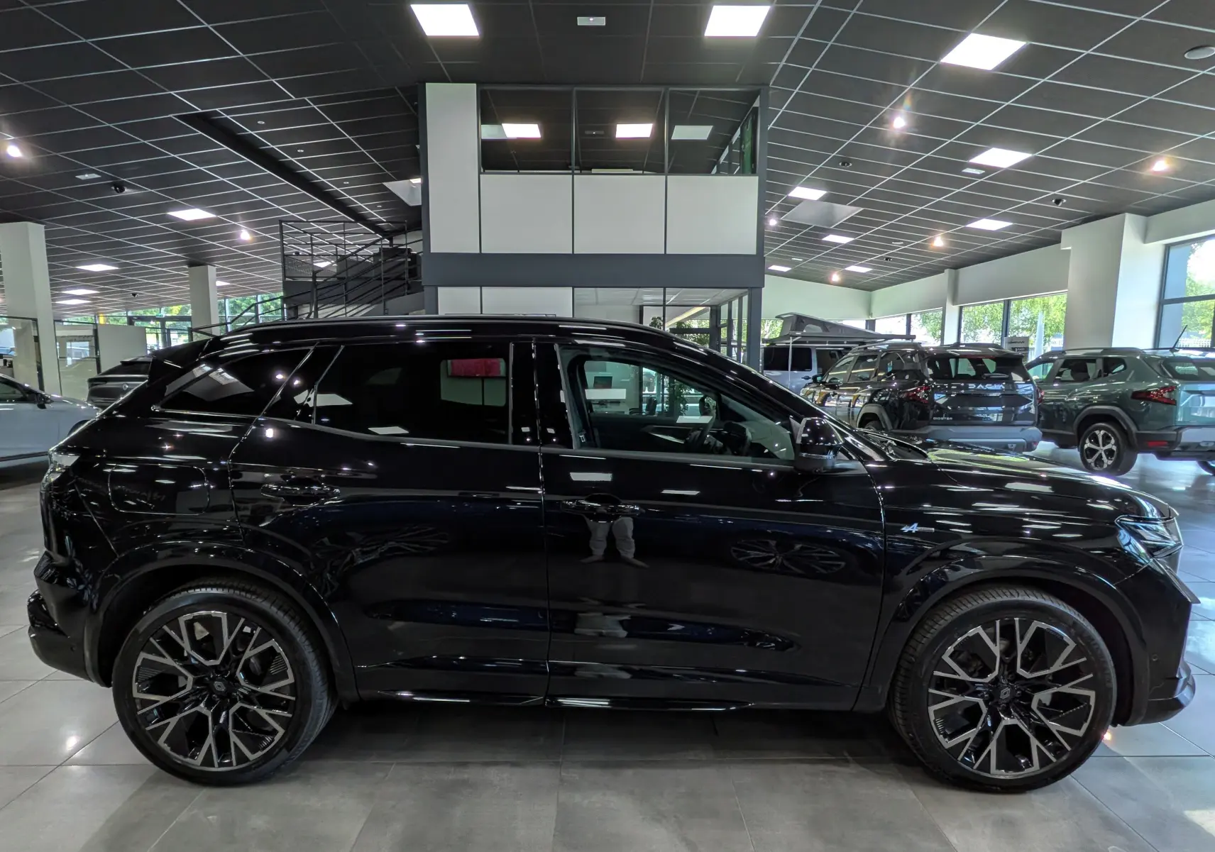 Profil côté gauche d'un Renault Austral noir full hybrid E-Tech 200 ch Esprit Alpine en showroom, avec jantes bi-ton distinctives.