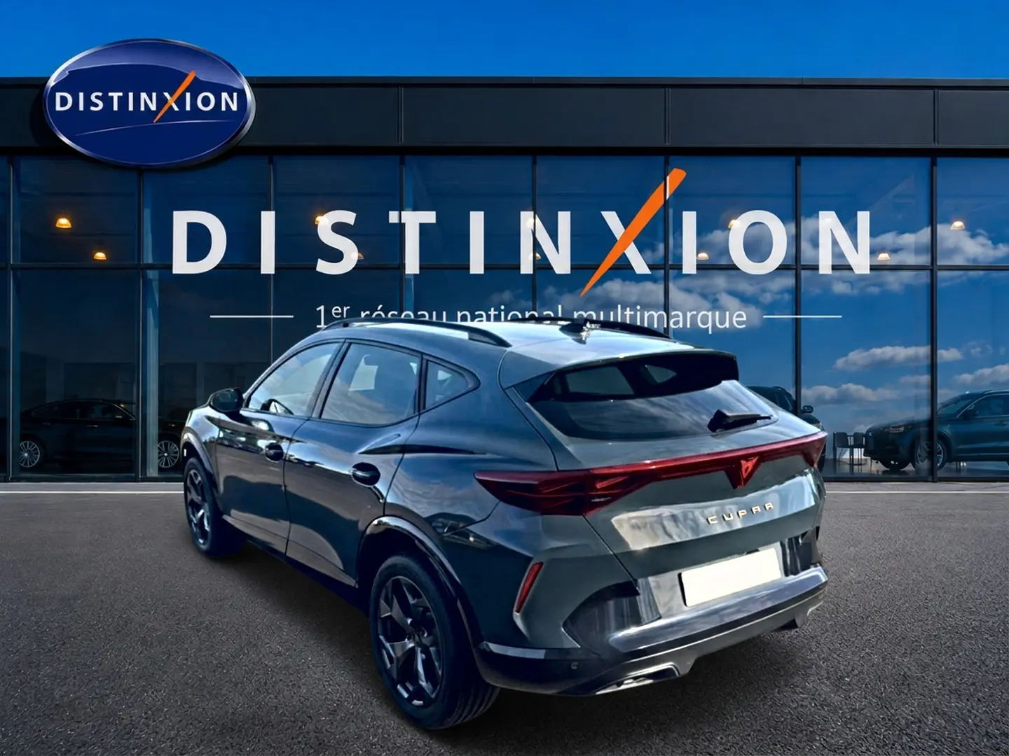 Vue 3/4 arrière droite d'un CUPRA Formentor bleu fjord avec feux arrière LED et jantes noires devant un showroom Distinxion.