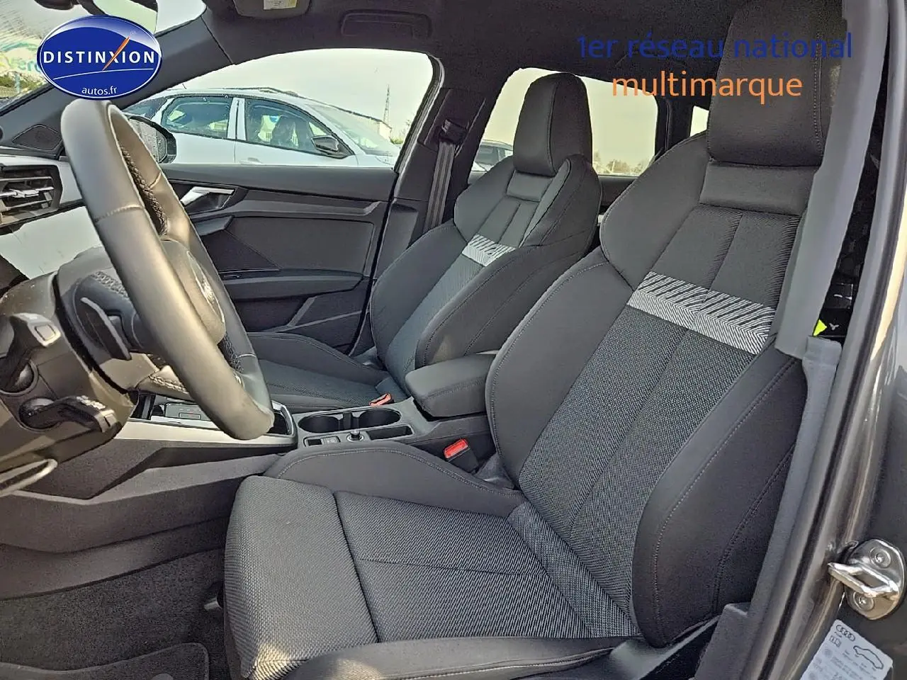 Intérieur avant de l'Audi A3 Sportback 2024, sièges sport noirs avec bande grise, volant cuir 3 branches visible côté gauche.