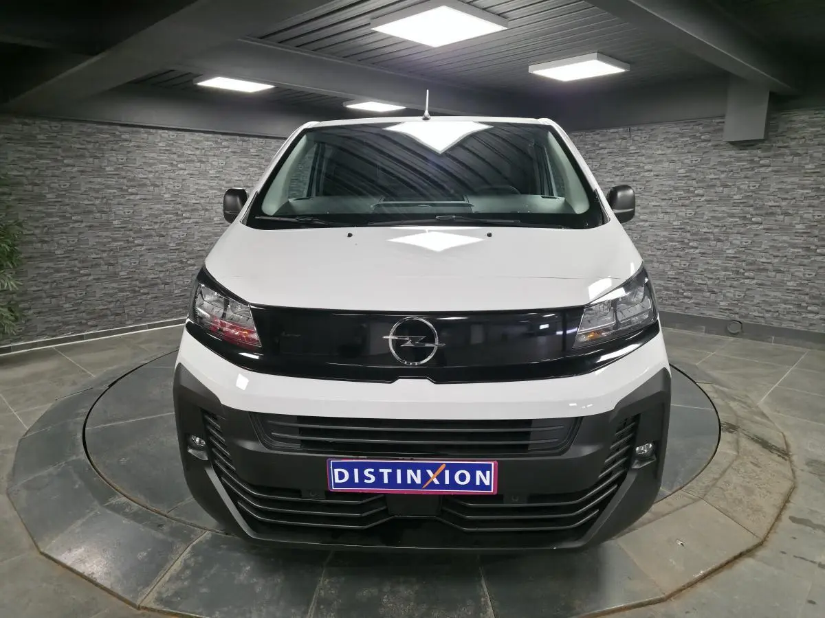 Vue avant d'un Opel Vivaro blanc 2025 avec calandre noire brillante et projecteurs intégrés, en intérieur showroom.