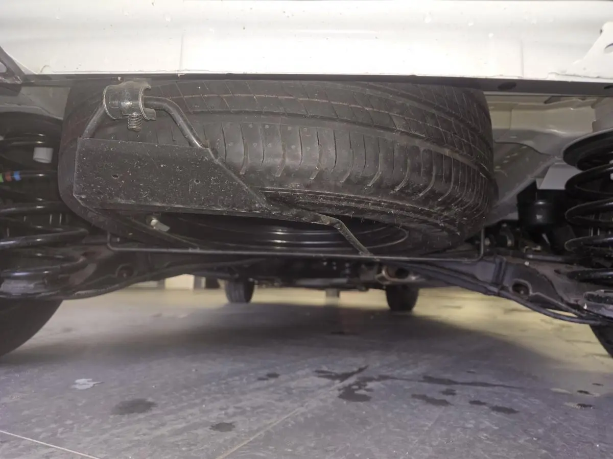 Vue en contre-plongée sous un Opel Vivaro blanc, montrant la roue de secours montée sous le châssis.