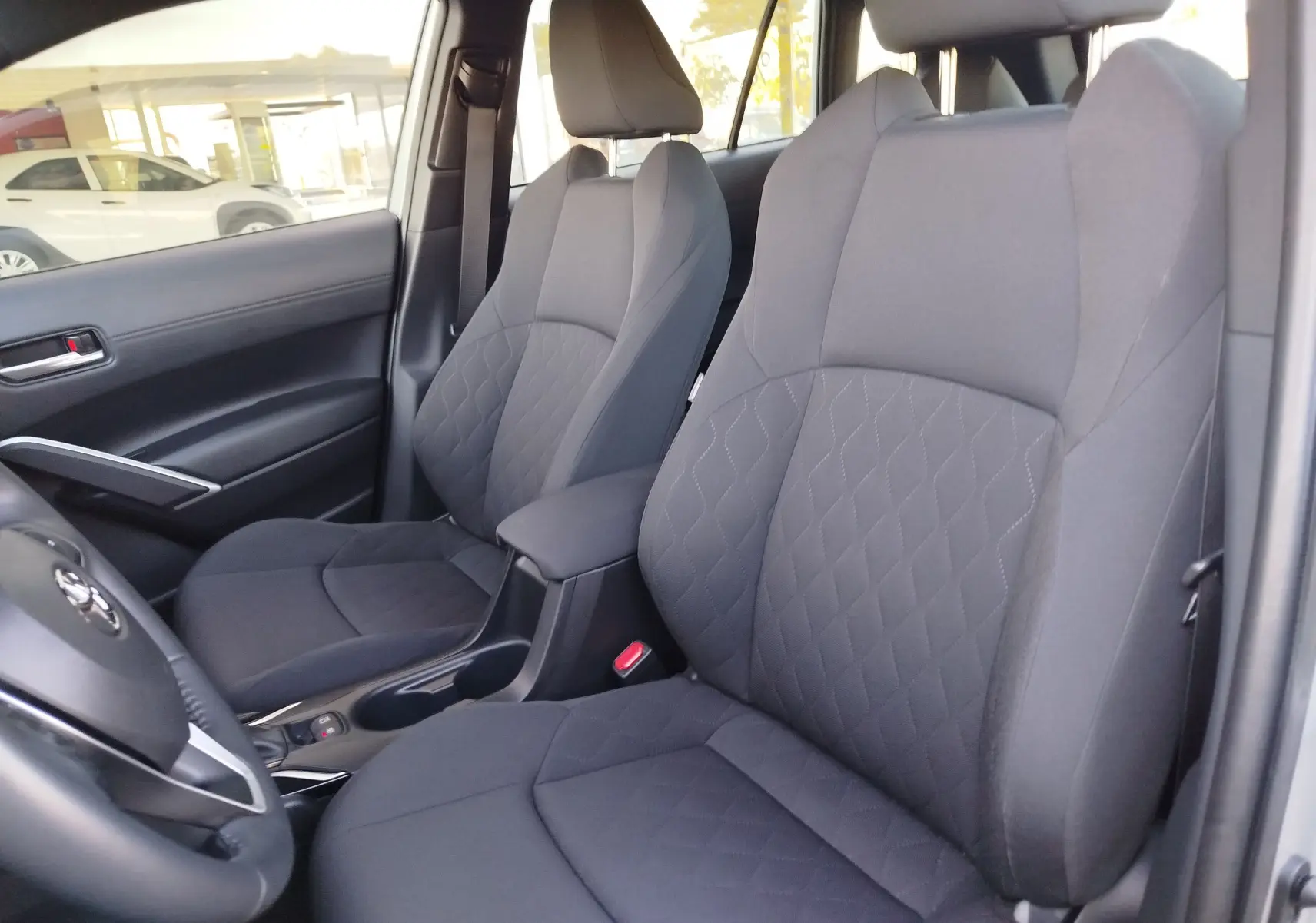 Vue intérieure côté conducteur du Toyota Corolla Cross 2025 gris minéral, mettant en valeur les sièges tissu gris avec surpiqûres losanges.