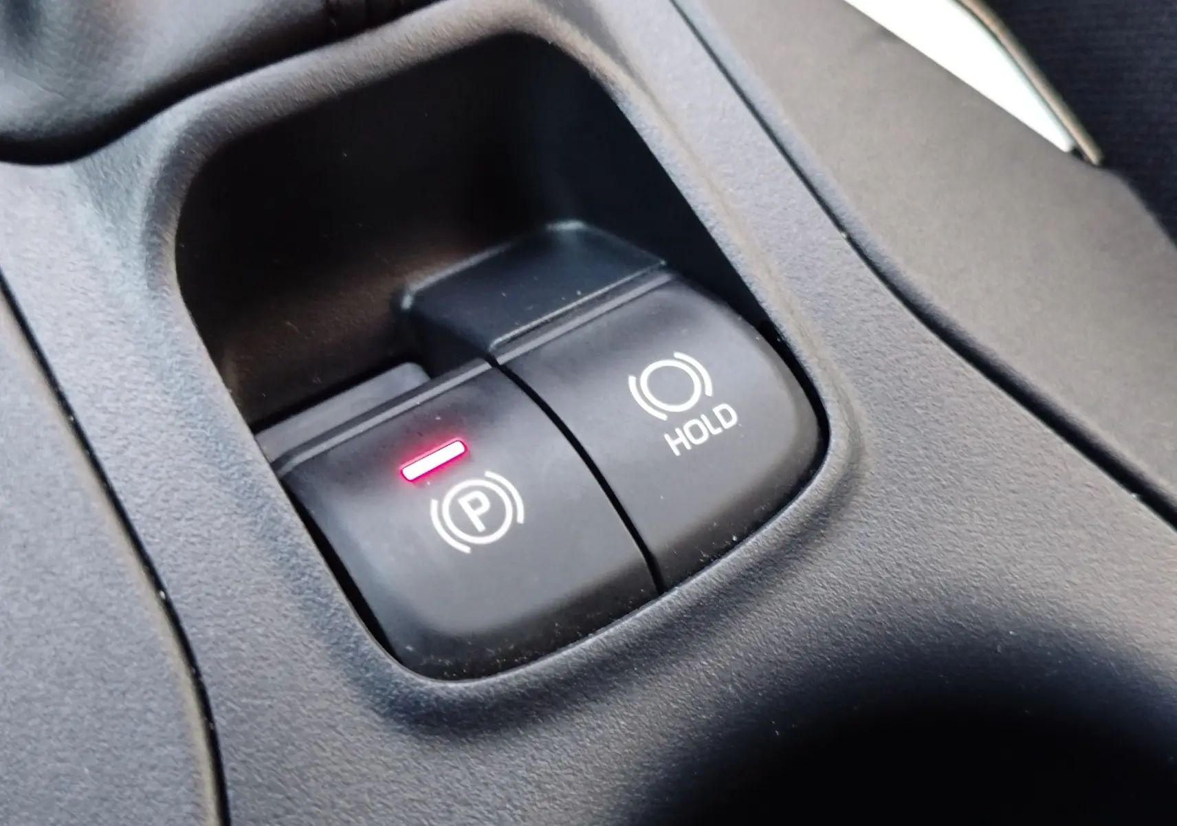 Gros plan sur les boutons de frein à main électronique et hold dans l'habitacle gris foncé du Toyota Corolla Cross 2025.