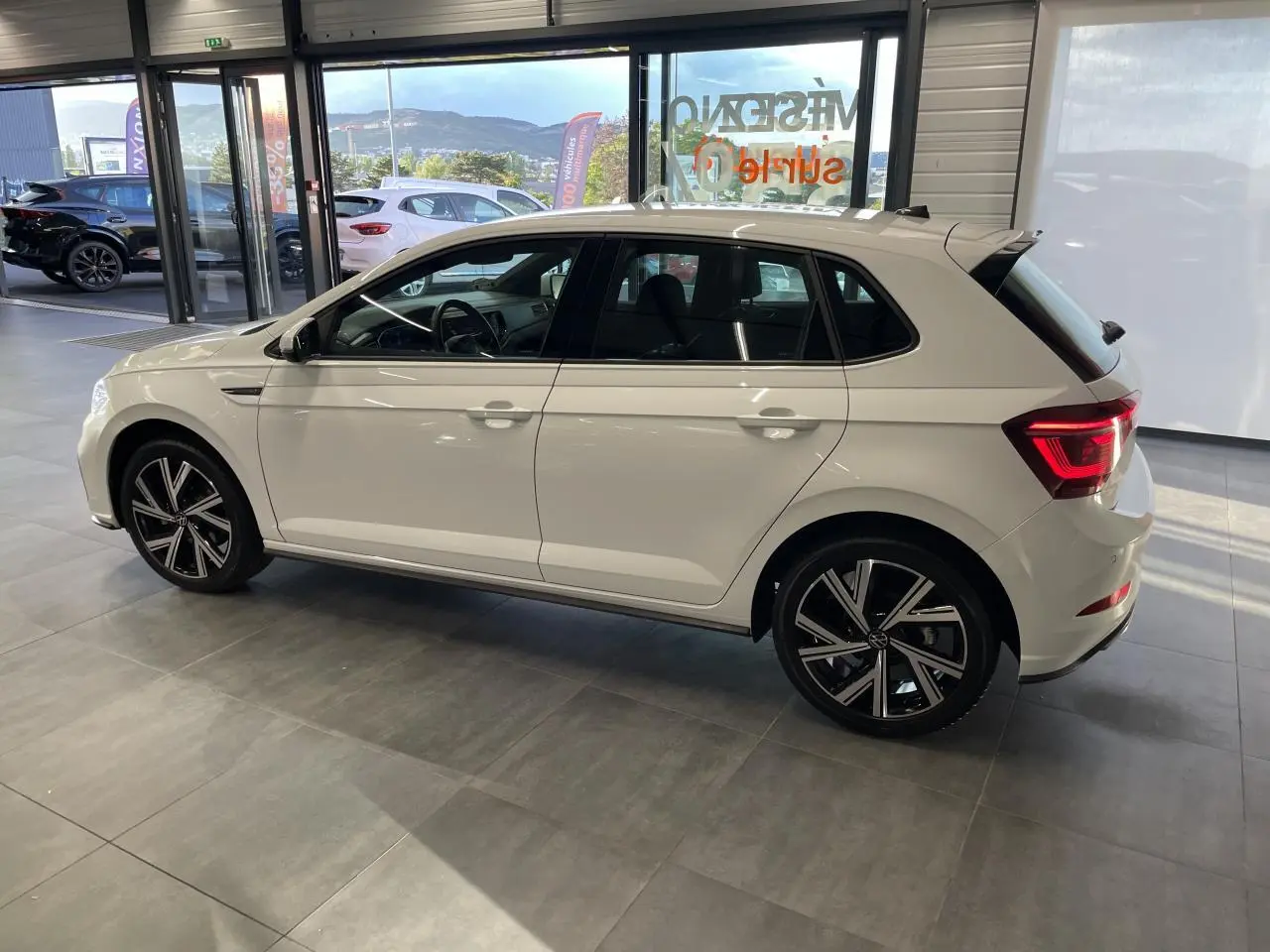 Volkswagen Polo 1.0 TSI R-Line blanche vue de profil côté gauche en intérieur avec jantes alliage noires et chromées.