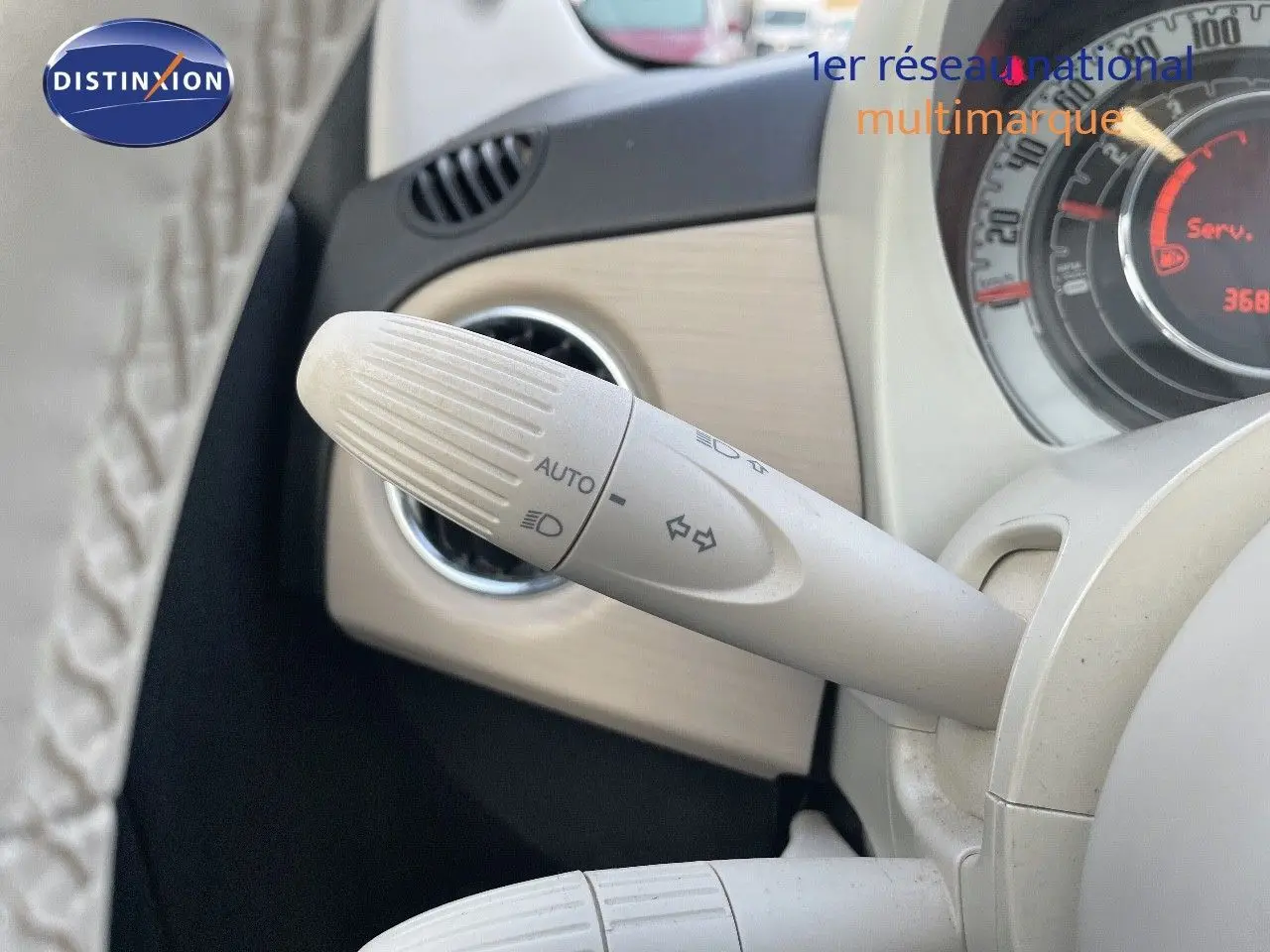 Gros plan sur la commande de clignotants blanche à gauche du volant d'une Fiat 500 blanche, tableau de bord partiellement visible.