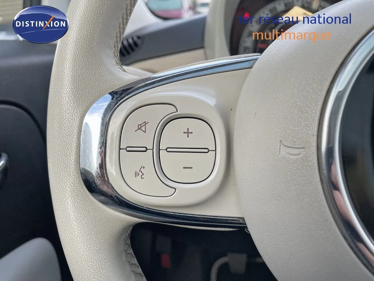 Gros plan sur les commandes blanches du volant cuir clair d'une FIAT 500 blanche, version 1.0 Hybrid 70CH DolceVita.