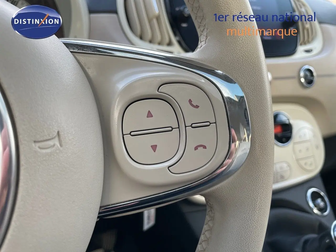 Gros plan sur les commandes du volant beige de la FIAT 500 blanche, mettant en valeur les boutons de gestion d'appels et navigation.