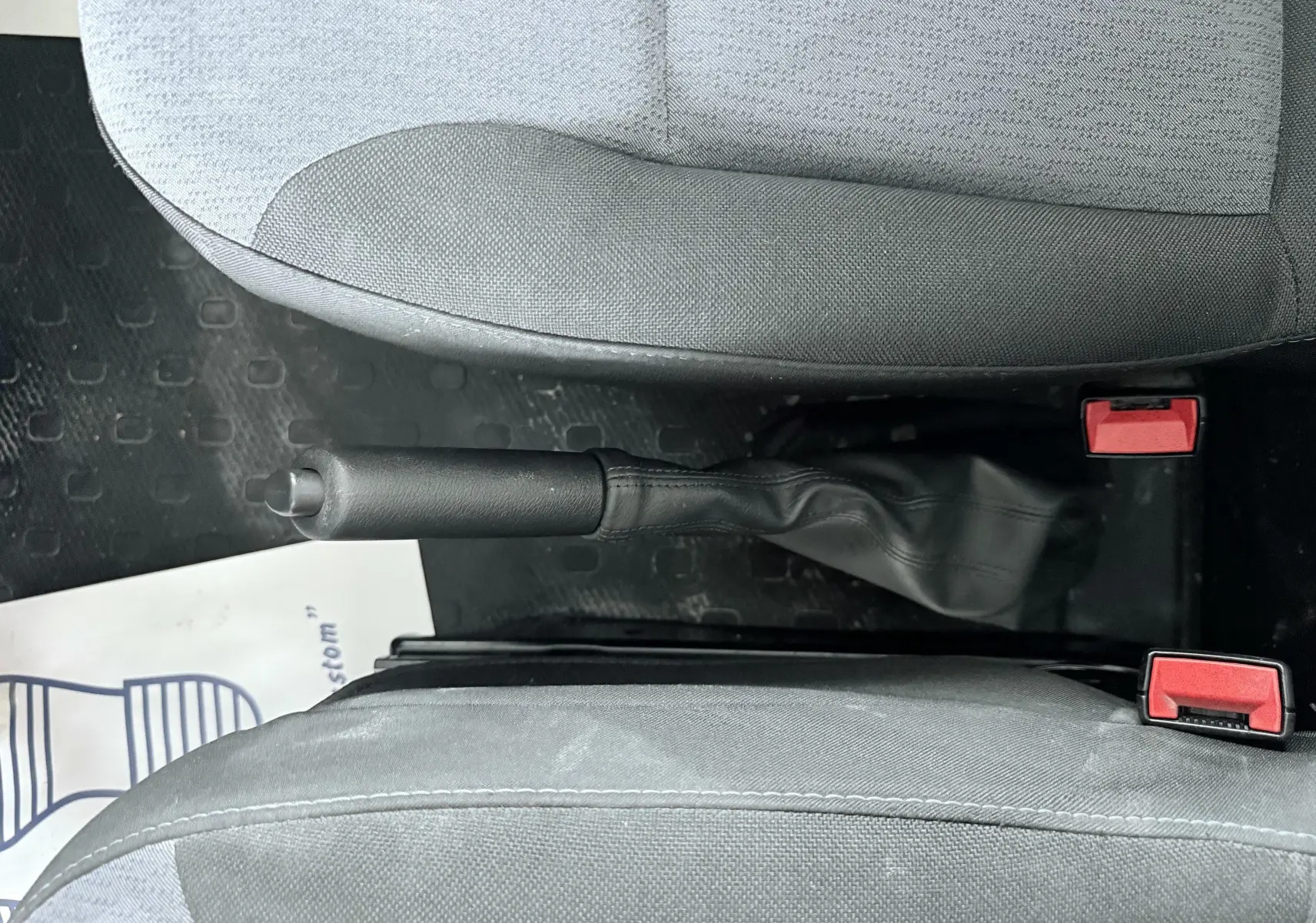 Vue intérieure centrée sur le frein à main entre les sièges avant gris du véhicule Opel Vivaro blanc.
