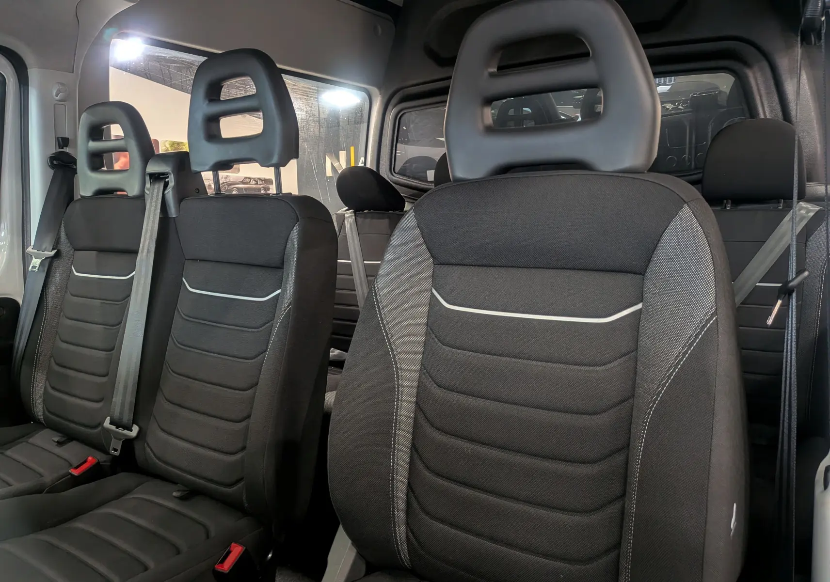 Vue intérieure sur les sièges en tissu noir du fourgon Iveco Daily 2025, montrant trois places avant avec appuie-têtes.