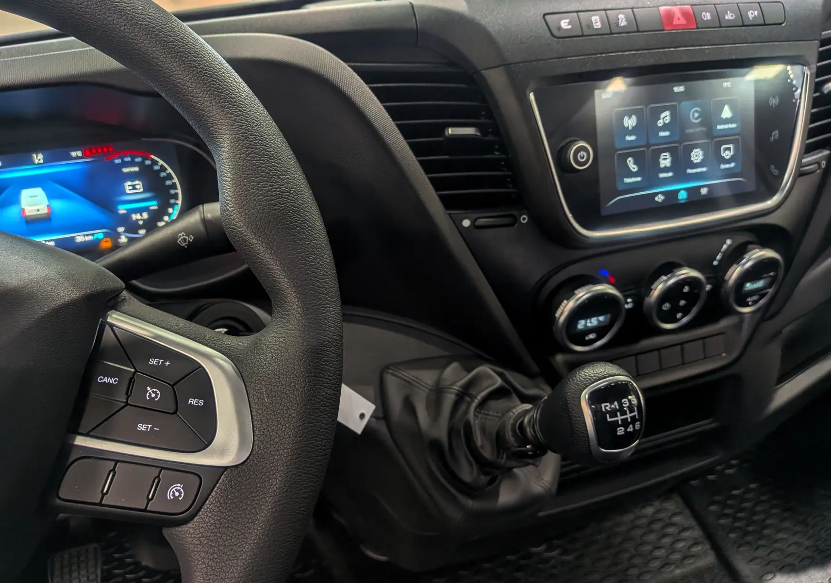 Vue rapprochée de l'intérieur du Daily Fourgon blanc 2025, montrant volant, levier de vitesses manuel et écran tactile central.