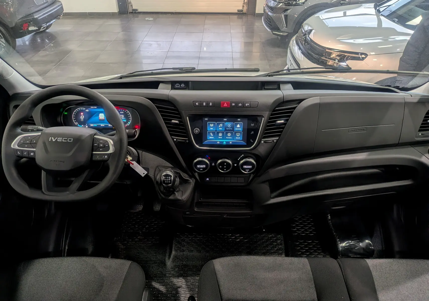 Vue intérieure avant du tableau de bord noir du fourgon Iveco Daily 2025 avec écran tactile et volant multifonction.