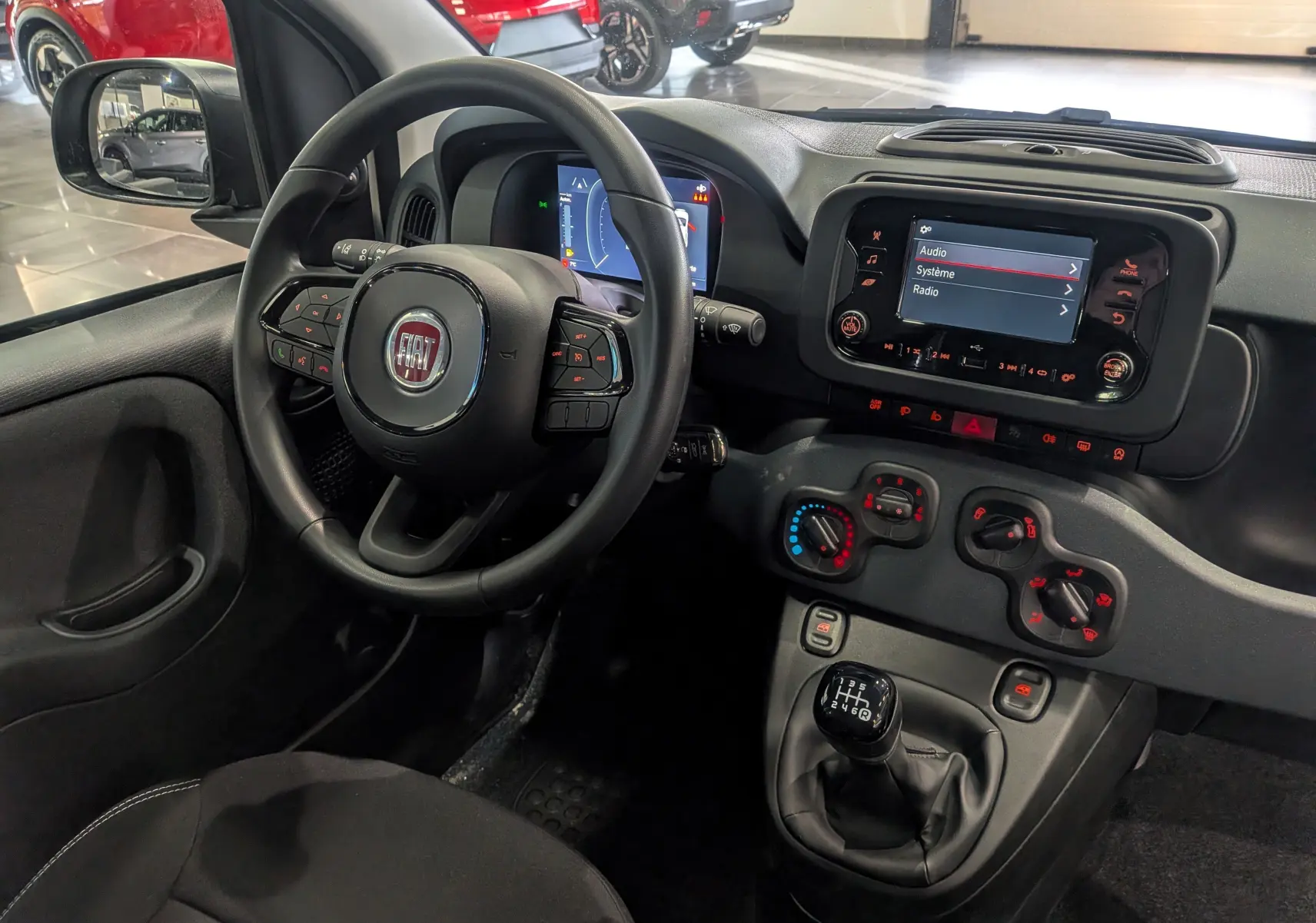 Vue intérieure côté conducteur de la Fiat Panda 1.0 Hybrid 2025, avec tableau de bord noir et écran tactile central allumé.
